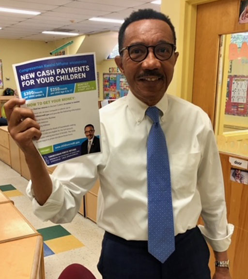 Congressman Kwesi Mfume holding a flyer announcing payments to parents.
